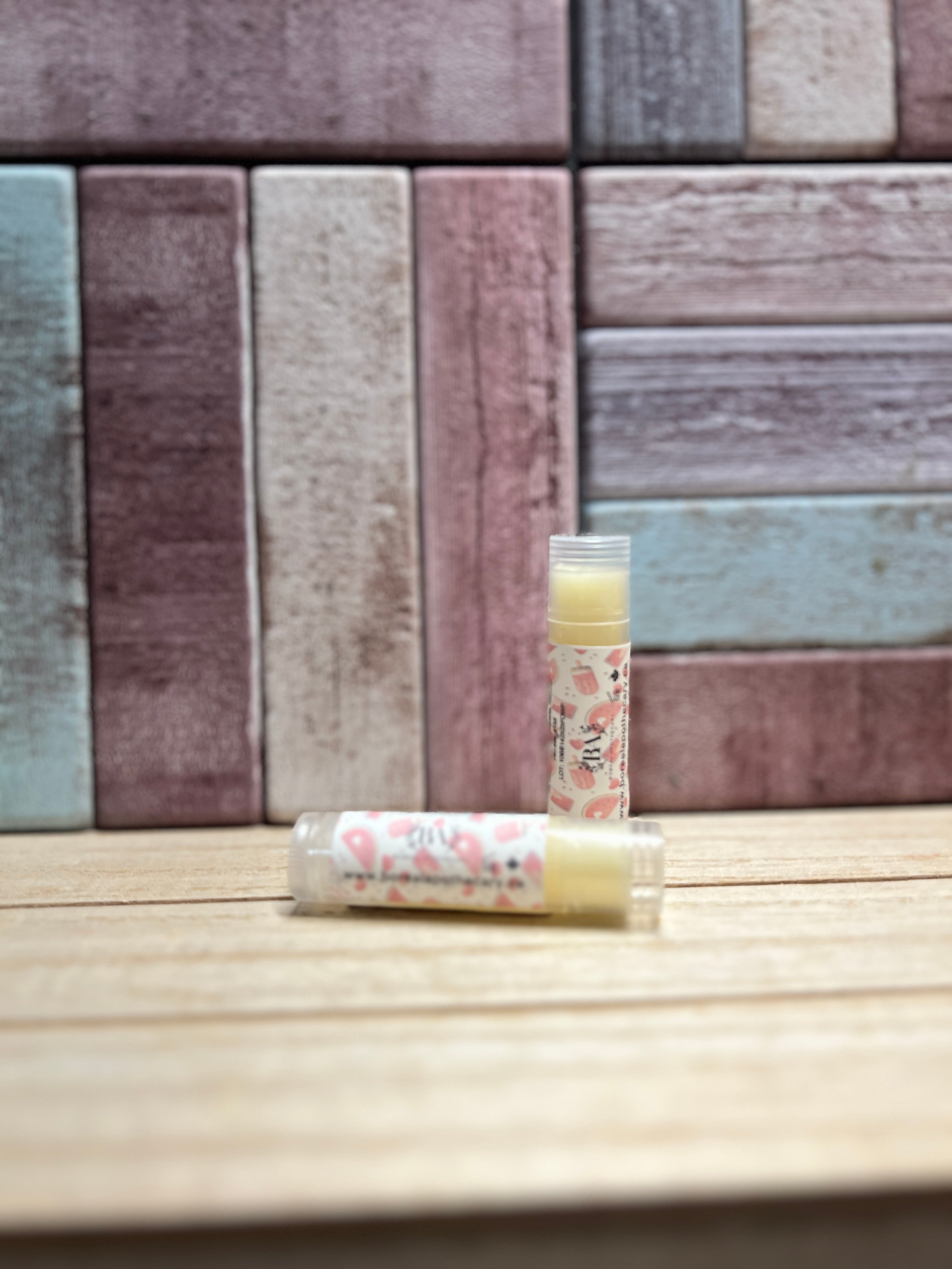 Two lip balms on a wooden surface with a patterned wall in the background