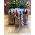 Colourful candles in paper wraps tied with twine on a wooden surface with flowers in the background.