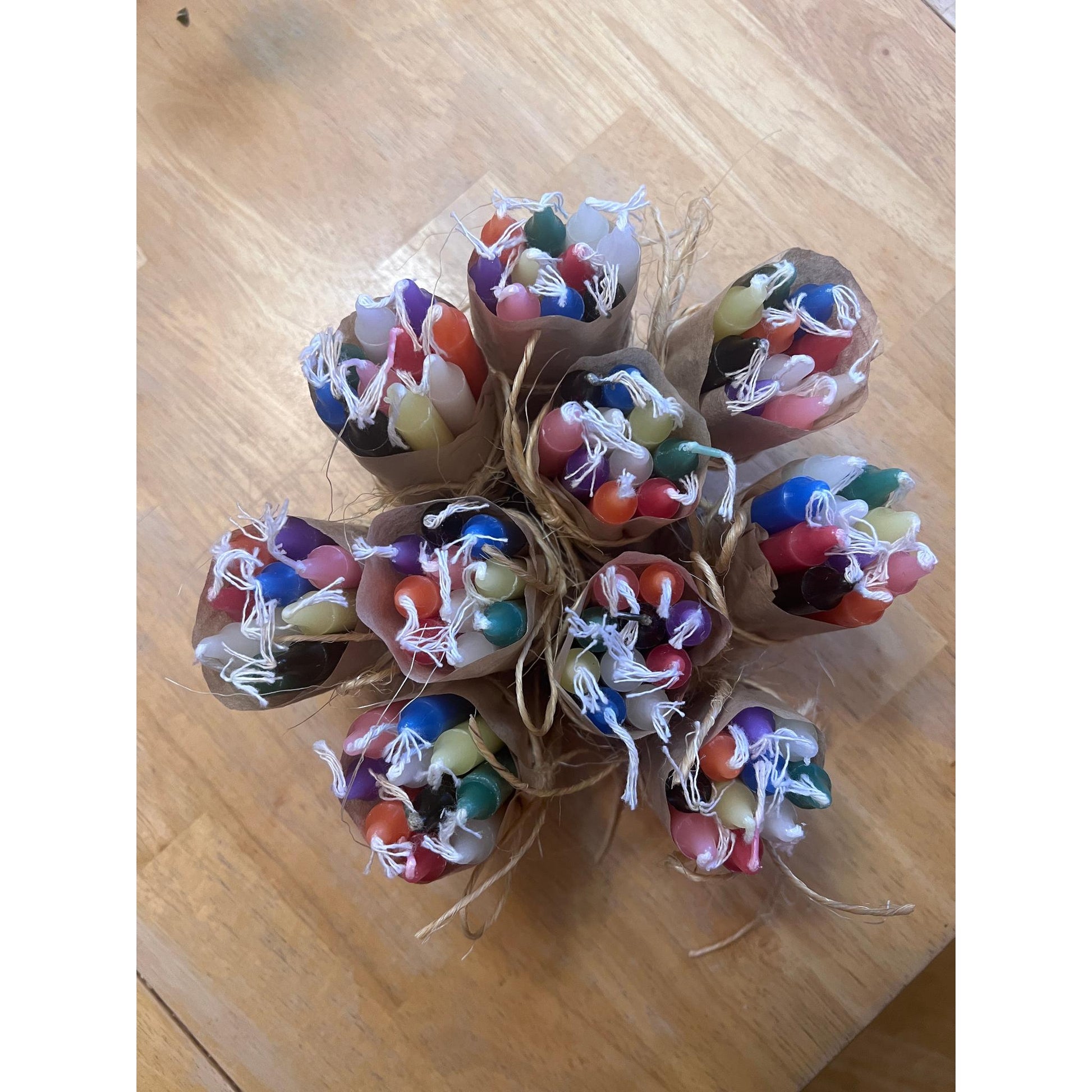 Colourful candles in paper wraps tied with twine on a wooden surface with a background.
