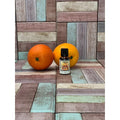 Two oranges and a small bottle on a wooden surface with a multicolored tile background