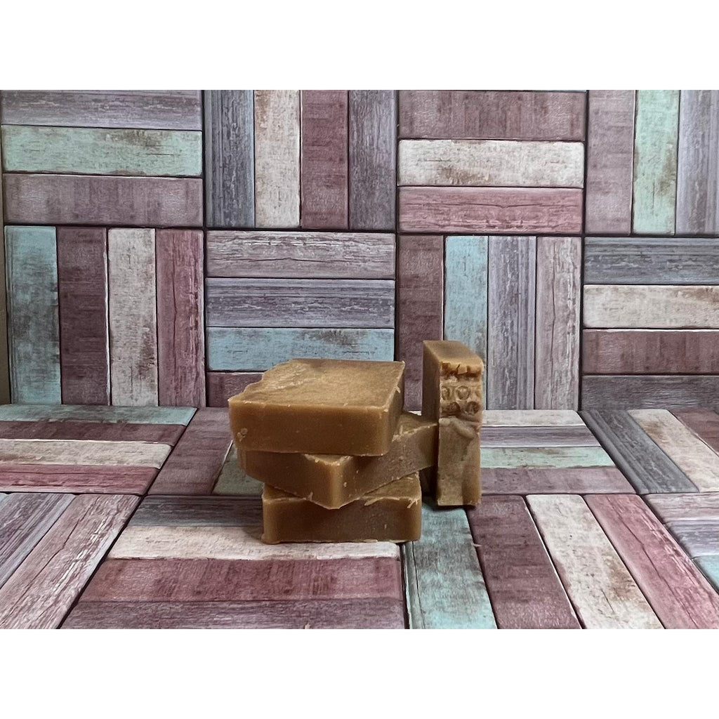 Three brown soap bars stacked on a wooden surface with a wooden wall background